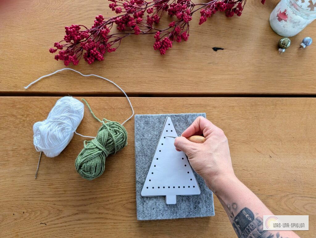 Hand mit Wollnadel näht Muster in Karton-Tannenbaum
